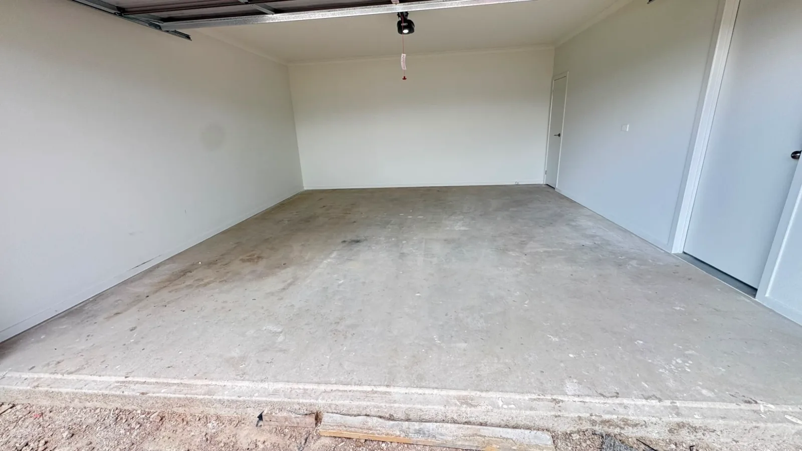 Bare builder's slab in an Officer double garage before epoxy flooring, with paint splatter and staining